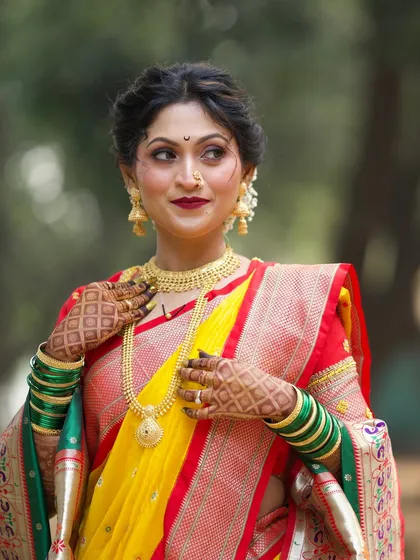 A stunning close-up of the bride. Her bold red lip and defined eyes are paired with traditional gold jewelry and a chandrakor bindi for a classic Maharashtrian look.
