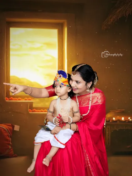 In this studio shot, a mother points towards a warm, glowing light from a window prop, sharing a story with her child dressed as Little Krishna. This setup creates a narrative feel, capturing a moment of discovery and wonder.