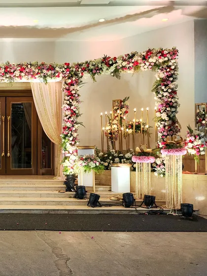 This grand entrance setup for a wedding ceremony features a large floral arch, candle stands, and traditional elements for a sacred and beautiful welcome.
