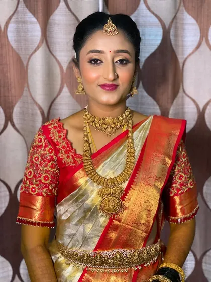 Bride Vidya embodies classic elegance for her Muhurtham. Her look features a traditional red and white silk saree, complemented by a clean makeup look with defined eyes and a rich lip color. This timeless combination is a specialty of mine, ensuring the bride looks stunning both in person and in photographs.