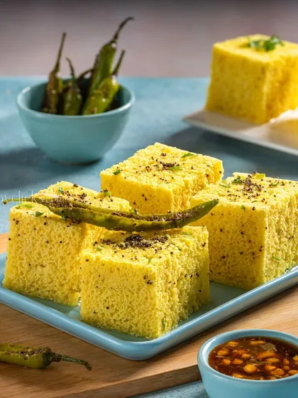 A plate of fluffy, yellow dhokla, shot for Gulab Sweets against a bright blue background.
