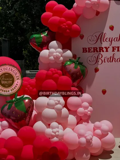 A close-up of a "Berry First Birthday" balloon arrangement, featuring shades of pink and red with strawberry-shaped foil balloons.