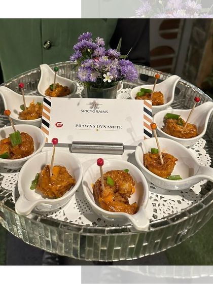 Dynamite Prawns served in elegant individual spoons on a mirrored tray. These crispy prawns are tossed in a creamy, spicy sauce for an unforgettable bite.