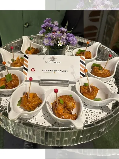 Dynamite Prawns served in elegant individual spoons on a mirrored tray. These crispy prawns are tossed in a creamy, spicy sauce for an unforgettable bite.