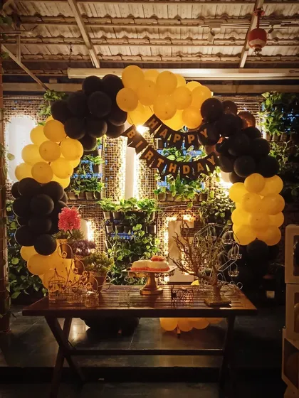A modern and stylish balloon arch in a striking yellow and black color scheme. Set against a natural green wall, this setup includes a 'Happy Birthday' banner and transparent 'BABY' blocks for a chic, contemporary feel.