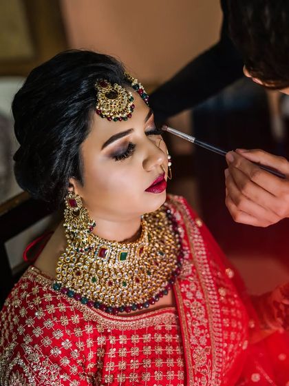The makeup artist applies the finishing touches to the bride's eyes. This close-up shot highlights the artistry and focus involved in creating the perfect bridal look.