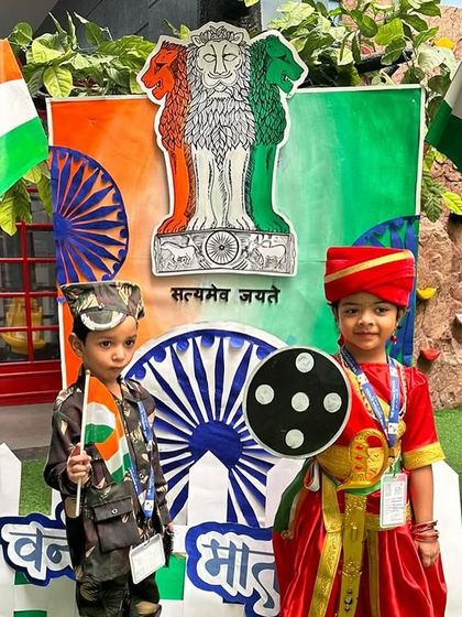 Two young students in patriotic costumes pose with the Indian flag, embodying the spirit of a free and proud nation.