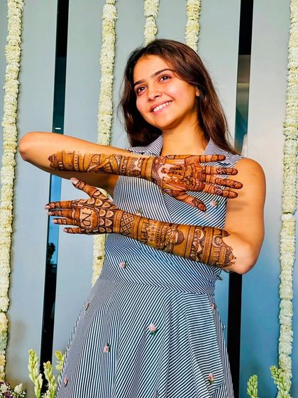 A happy client posing with her full-arm mehandi, personalized with her initials.