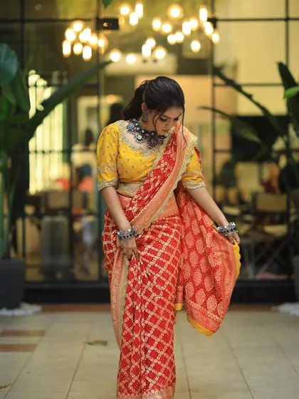 A full view of the model in her beautiful red and yellow saree, with her hair styled in a chic, wavy ponytail.