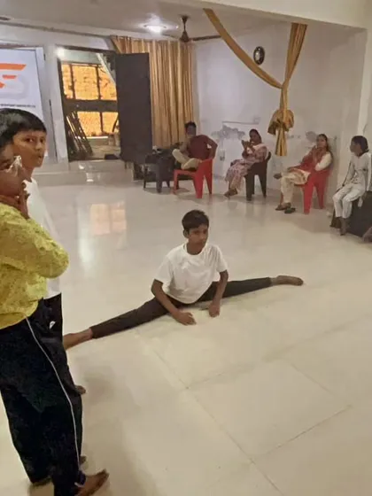 A young student demonstrates a full split in the middle of the training hall while others watch. He is an inspiration to his peers.