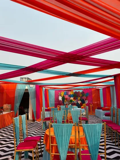 A wide view of a Mehandi event space, showing the colorful ceiling drapes, chevron flooring, and coordinated seating arrangements that create a cohesive and festive atmosphere.