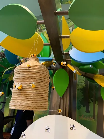 A close-up of a beehive prop hanging from a tree, a small detail that adds to the immersive Hundred Acre Wood theme.
