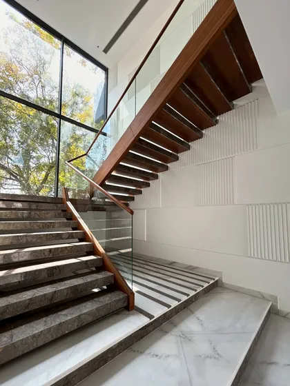 A view up the Gulmohar Farmhouse staircase, with the large window framing the trees outside. The glass railing ensures an unobstructed view and a feeling of lightness.