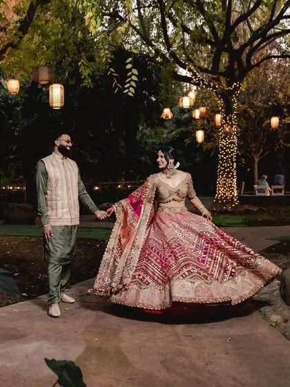 A romantic shot of the couple, with the festive lights creating a magical glow. Her vibrant lehenga and his coordinated olive green kurta create a stunning pair.
