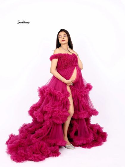 A glamorous full-length portrait of a mother-to-be in a magenta ruffled gown. Her confident pose and the stunning dress create a high-fashion maternity look.