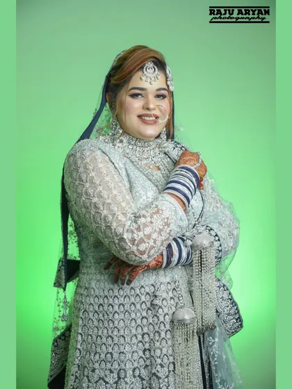 A beautiful portrait of a Muslim bride on her Nikah day. Her elegant pose and traditional white and blue attire are highlighted against a simple green studio background.
