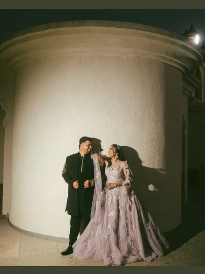 A night portrait of Ayush and Sakshi. The dramatic lighting against the curved wall creates a modern and moody atmosphere, highlighting their elegant attire and the chemistry between them.