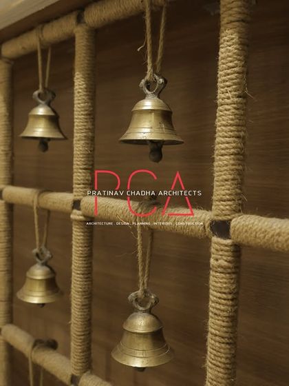 A close-up of a decorative element within the fashion studio: a wall feature made of jute rope and hanging brass bells, evoking the serene and spiritual atmosphere of Indian temples.