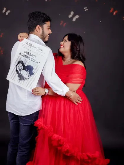 A creative announcement shot. The mom-to-be embraces her partner, who has a "Our Baby is Coming Soon" newspaper print on his back.