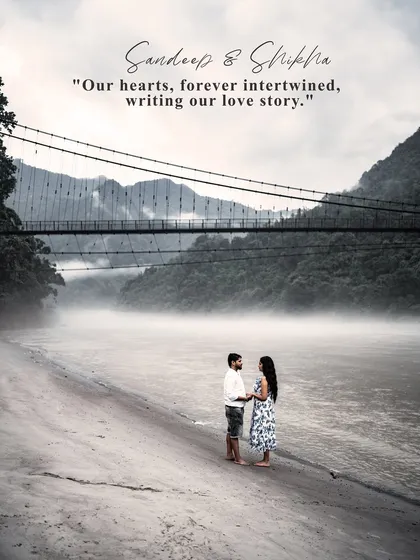 An iconic pre-wedding photograph of a couple standing on the banks of the Ganga in Rishikesh, with a misty suspension bridge in the background. This wide-angle shot captures both the scale of the landscape and the couple's connection.