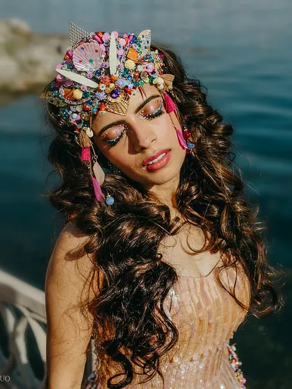 A beautiful close-up of the bride, showing off her intricate, handmade headpiece made of shells, beads, and feathers, and her vibrant, festival-inspired makeup.