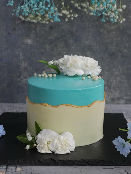Simple elegance is always in style. This fault line cake combines a clean white base with a vibrant turquoise top, accented with delicate white carnations for a sophisticated look.