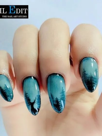 A beautiful example of landscape nail art. This design captures a serene forest silhouette against a dusky teal sky, showcasing our ability to create atmospheric and detailed scenes on a small scale.