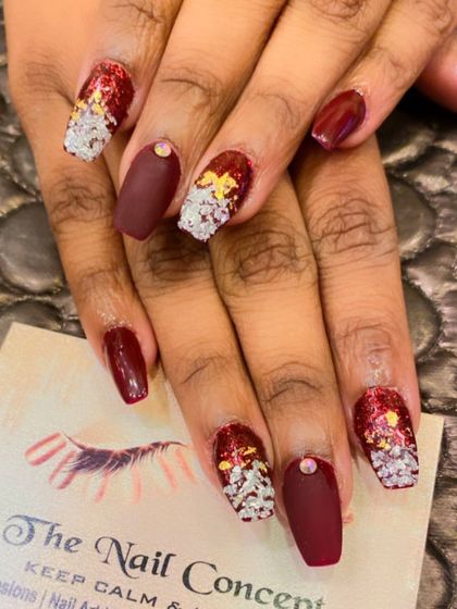 A dramatic and textured design on square nails. This set combines matte and glossy maroon polish with accent nails featuring a chunky, textured silver and gold glitter effect.