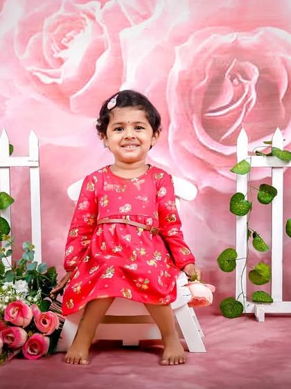 A sweet smile from this little girl, sitting in front of a pink floral backdrop with a charming white picket fence. A perfect studio portrait.