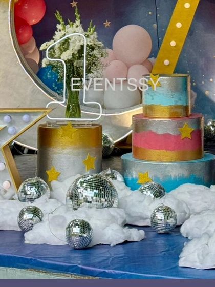 A close-up of the themed cake and the illuminated number "1" prop, surrounded by fluffy "clouds" and mini disco balls.