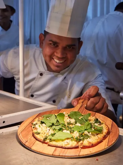 A happy chef presenting a freshly baked pizza straight from the oven. This image captures the pride and joy our team takes in serving delicious food to your guests.