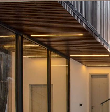 A detail of the ceiling and window frames, showing the clean lines of the linear lighting integrated into the wooden ceiling slats.