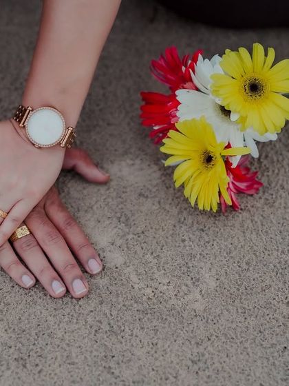 A detail shot of the couple's hands resting on the sand next to a small bouquet of colorful flowers, symbolizing the simple, beautiful moments of their love story.