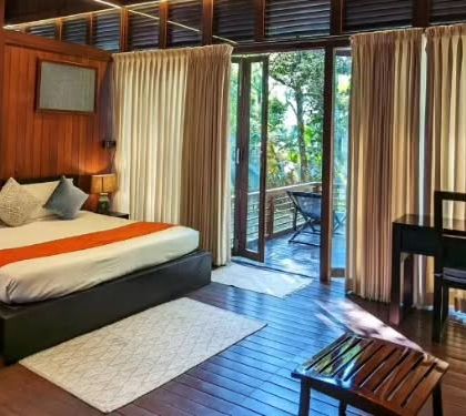 The interior of an elegant nature lodge in Coorg, featuring warm wooden tones and a private balcony. It's the perfect cozy retreat after a day of exploring the coffee plantations.