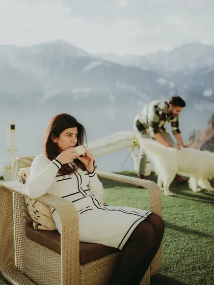 A candid moment of the bride-to-be enjoying her tea, with her partner and their dog in the background against a mountain vista.