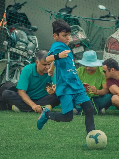A young player dribbles the ball while parents watch from the sidelines.