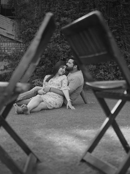 An artistic black and white pre-wedding photo, framed through two chairs, creating a sense of intimacy and a unique perspective.
