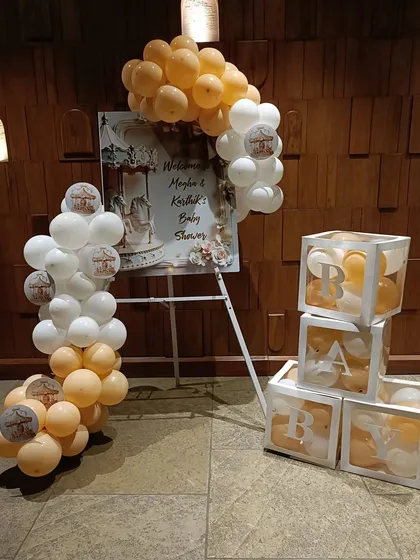 A classic baby shower setup featuring a welcome sign and "BABY" blocks filled with balloons. The soft peach and white color scheme is perfect for a gender-neutral or surprise celebration.