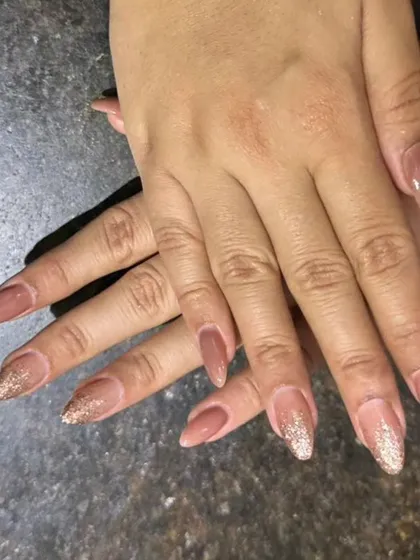 A sophisticated ombre design blending a nude base into a sparkling rose gold glitter tip on pointed almond nails.