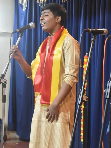A student vocalist sings with passion during our Kannada Rajyotsava celebration. He wears the traditional yellow and red sash to honor the occasion.