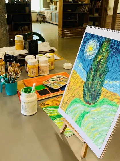 The setup for our Van Gogh workshop, with paints, brushes, and a reference painting of "Wheat Field with Cypresses."