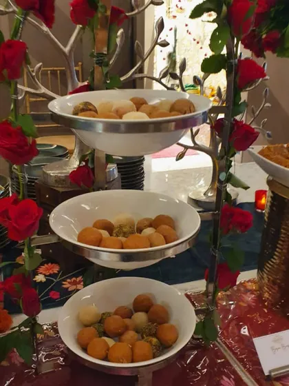 A three-tiered stand filled with a variety of Indian sweets. The vibrant red roses woven through the stand make this dessert display a true showstopper.
