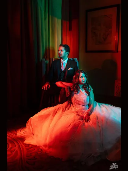 A regal portrait of the couple seated, bathed in dramatic red and green light for a cinematic reception look.