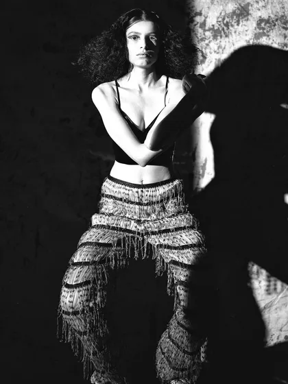 A high-contrast black and white image from the same series. The model's strong pose and the dramatic shadows create a powerful, graphic composition.