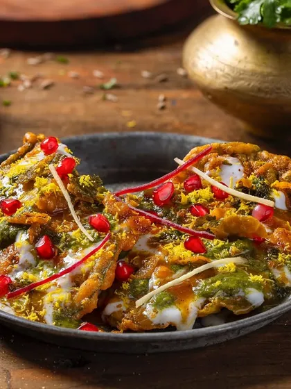 A plate of Papdi Chaat for Chhappan Bhog, garnished with pomegranate seeds and ginger. The close-up shot captures the layers of yogurt, chutneys, and crispy papdi.