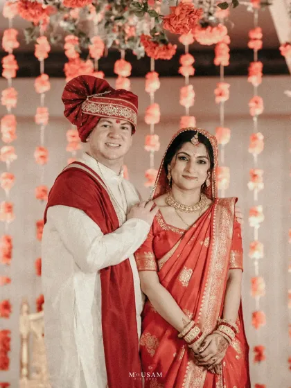 A portrait of a beautiful couple from different cultures, perfectly complementing each other in their red and white wedding attire. Their happy smiles show the joy of two families and traditions coming together.