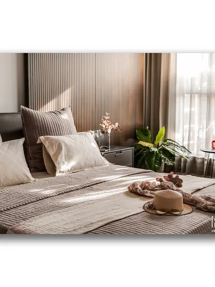 Sunlight streams into this cozy bedroom, highlighting the textures of the bedding and the fluted wood paneling behind the bed. The scene is warm and inviting, capturing a perfect lazy morning moment.