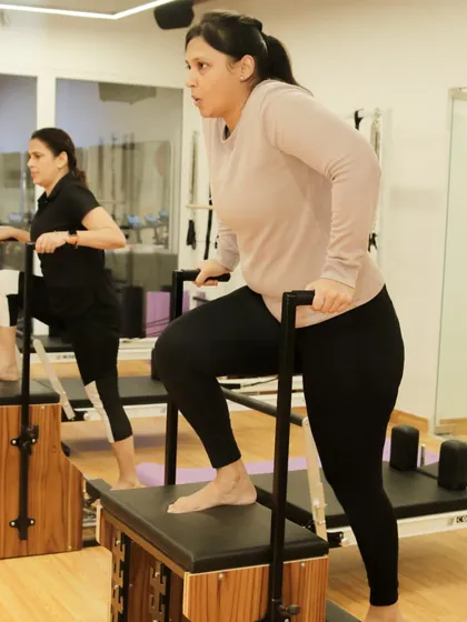 Two clients work in sync on the Pilates chair, showing the motivating atmosphere of our group classes.