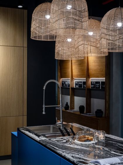 A bold blue island with a dramatic stone countertop is a highlight of our Ahmedabad showroom. The oversized wicker pendant lights add a touch of organic texture.