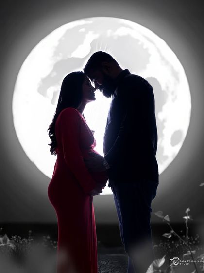 A black and white silhouette of a couple in front of the moon backdrop, creating a classic and artistic pregnancy portrait.